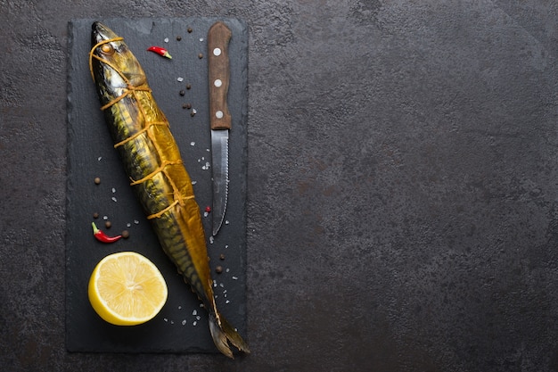 Smoked mackerel, knife and lemon on black stone cutting board, copy space.