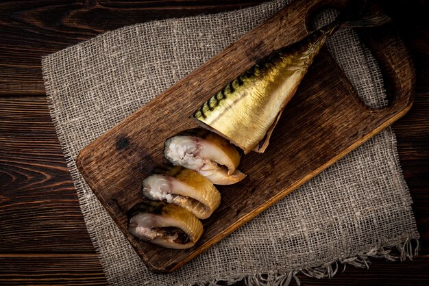 Smoked mackerel on wooden board on dark wooden table.