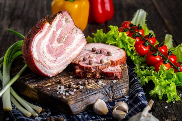 копченое мясо или свинина с салом, нарезанные, помидоры черри, травы деревенские, на черном деревянном, нарезка