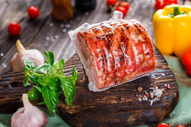 smoked meat or pork with lard, sliced, cherry tomatoes, herbs and spices, on a black wooden, cutting