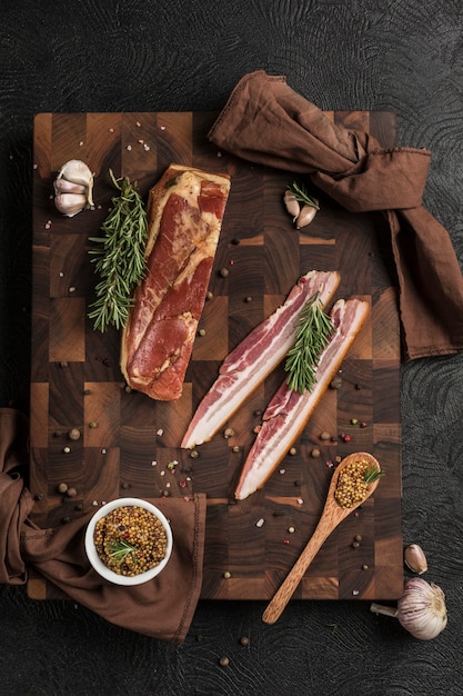 Photo smoked pork brisket on a wooden board with grainy mustard and fresh herbs on a dark background. top view. vertical orientation with a copy space for the text.