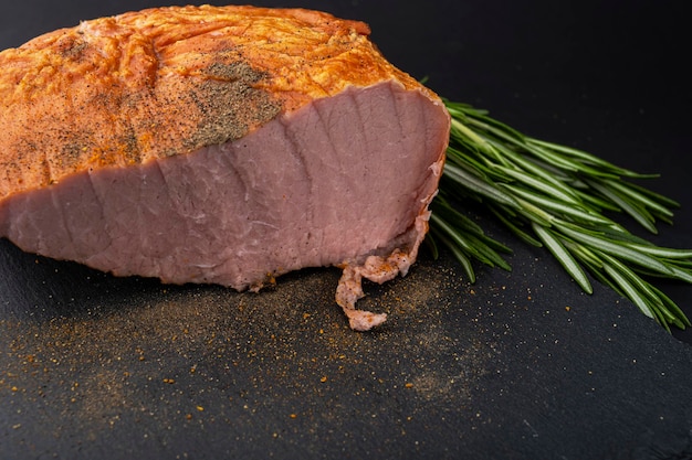 Smoked pork loin with spices, lies on a black tabletop.