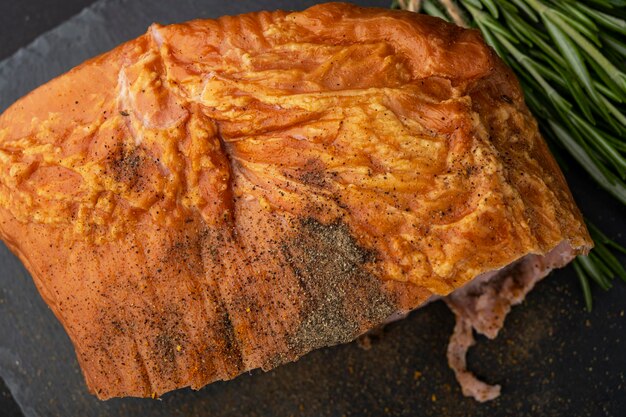 Smoked pork loin with spices, lies on a black tabletop.