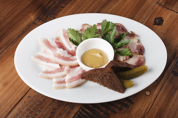 Smoked and salted lard on a white oval plate. bacon with sauce and greens. cold meat appetizer. wooden background.