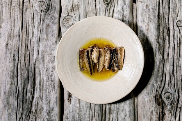 Smoked sardines in oil served in white ceramic plate over old grey wooden surface. Top view, flat lay. Copy space