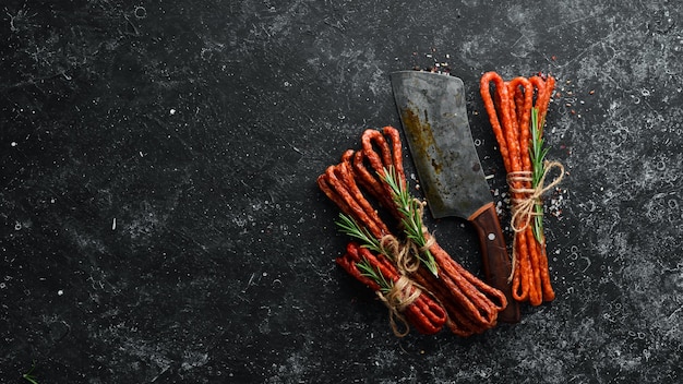 Smoked sausages on a black stone background Kabanosy Top view Free space for your text