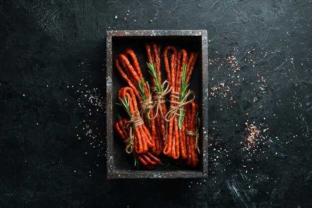 Smoked sausages on a black stone background Kabanosy Top view Free space for your text