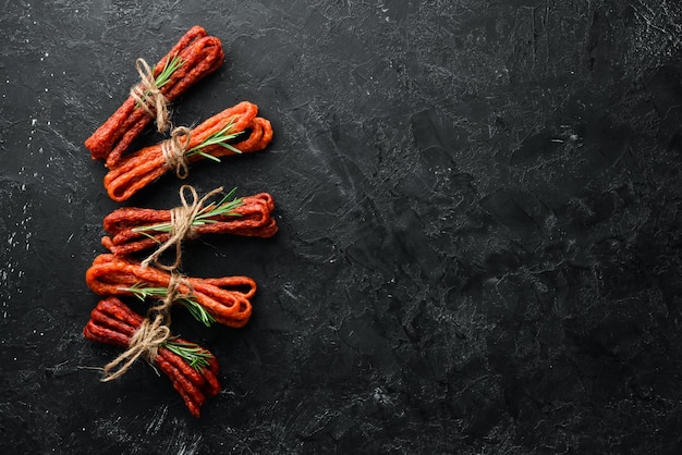 Smoked sausages on a black stone background Kabanosy Top view Free space for your text