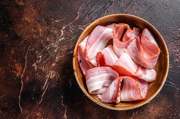 Smoked sliced bacon in wooden plate. Dark background. Top view. Copy space.