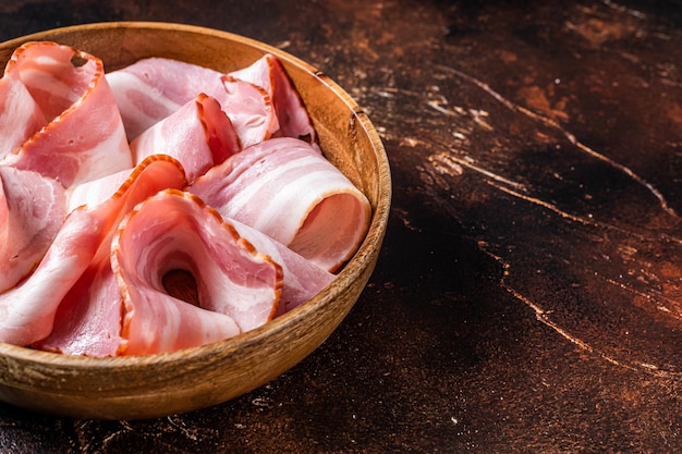 Smoked sliced bacon in wooden plate Dark background Top view Copy space