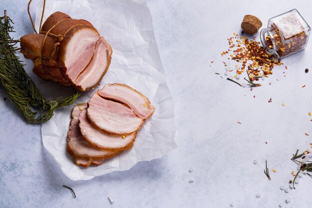 Photo smoked spicy pork roll on white parchment cut into slices surrounded by spices and herbs