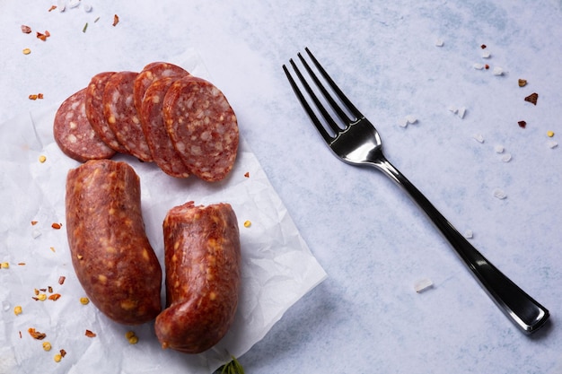 Photo smoked spicy sausage with cheese on white paper surrounded by spices and herbs on a light background