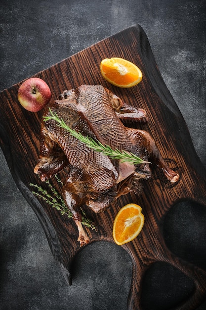 Smoked whole duck on a wooden board on a gray background with apples oranges rosemary and thyme