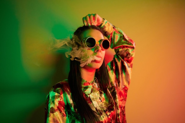 Smoking activity Fashionable young woman standing in the studio with neon light