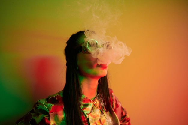 Smoking activity Fashionable young woman standing in the studio with neon light