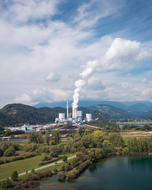 Smoking chimney at thermal power plant near lake and green nature aerial view