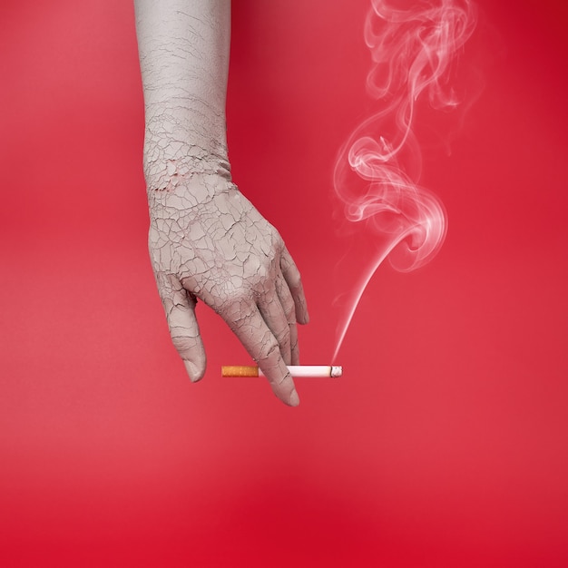 Smoking cigarette in a dry and cracked hand, bad effects of smoking on skin.