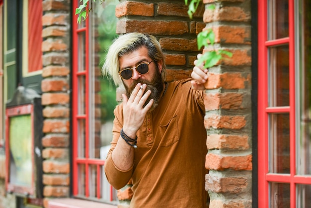 Fumare all'aperto andato in pausa fumo abitudine al fumo uomo maturo alla moda con la sigaretta occhiali da sole ragazzo brutale fumare tabacco ragazzo cool rilassante hipster che fuma vecchia architettura sfondo