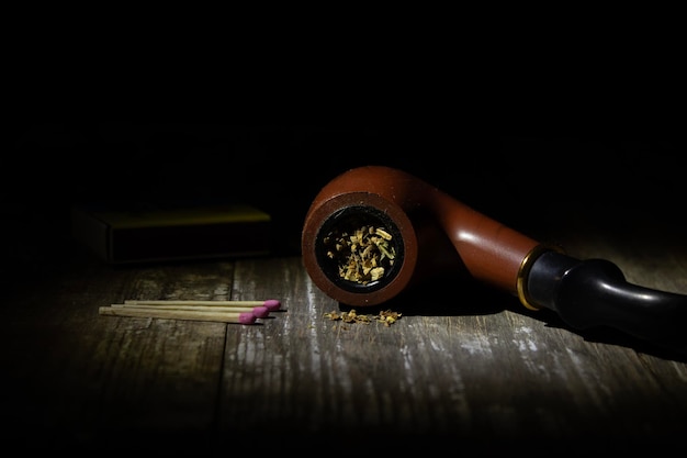 A smoking pipe filled with tobacco on a rough table against a dark background in a spot of light