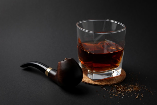 Smoking pipe tobacco and glass of alcohol on black\
background