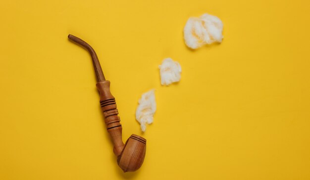 Smoking pipe with decorative clouds of smoke on a yellow