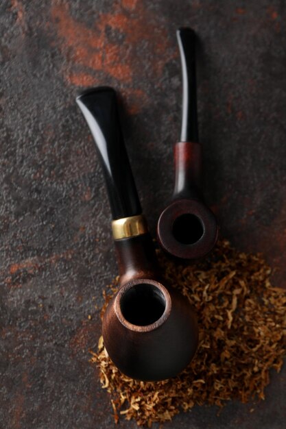 Smoking pipes with tobacco on dark textured background