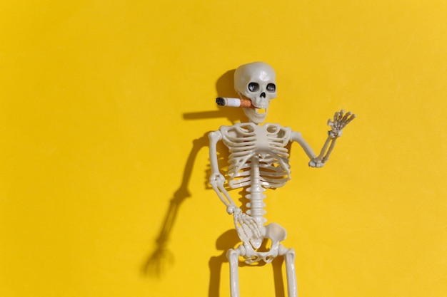 Smoking skeleton with a cigarette in the mouth against a bright yellow background. Smoking kills