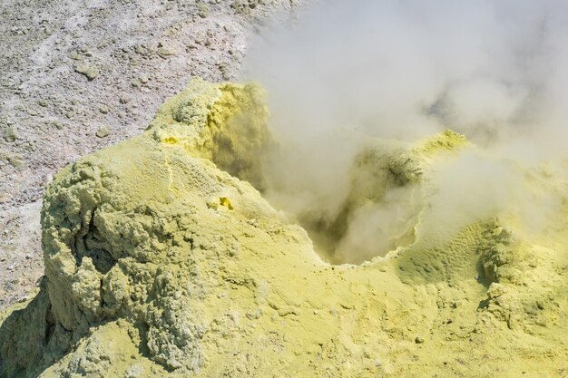 火山の斜面にある硫黄堆積物の間でソルファタラを吸う