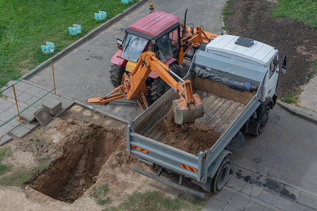 Smolensk Russia 08152018 a tractor with a backhoe digs a pit and loads of sand a dump body