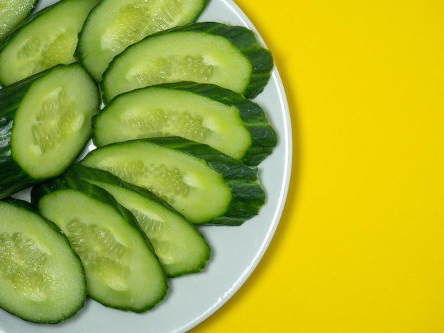 A smooth mediumsized cucumber on a plate sliced Cucumber on a yellow background