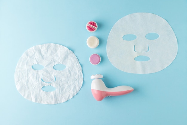 Smoothed and crumpled face masks and massager on a blue background. The concept of a rejuvenating effect on the skin.