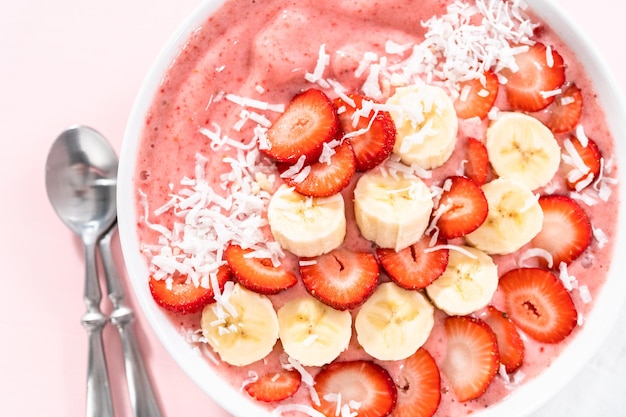 Smoothie bowl van aardbei en banaan gegarneerd met kokosvlokken en vers fruit