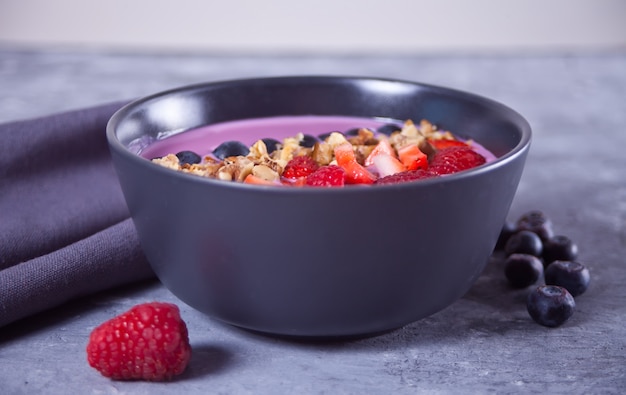 Smoothie bowl with berries and muesli on the gray table.