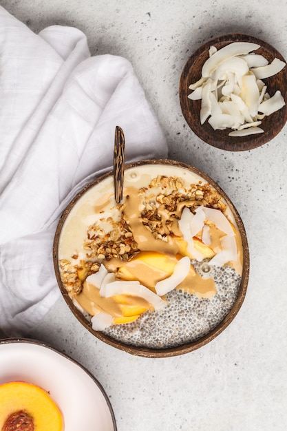 Smoothie bowl with chia pudding, peach, coconut and granola in a coconut bowl. Vegan healthy breakfast, clean eating concept.