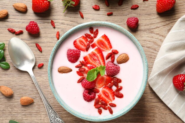 Smoothie bowl with goji berries and spoon on wooden table flat lay