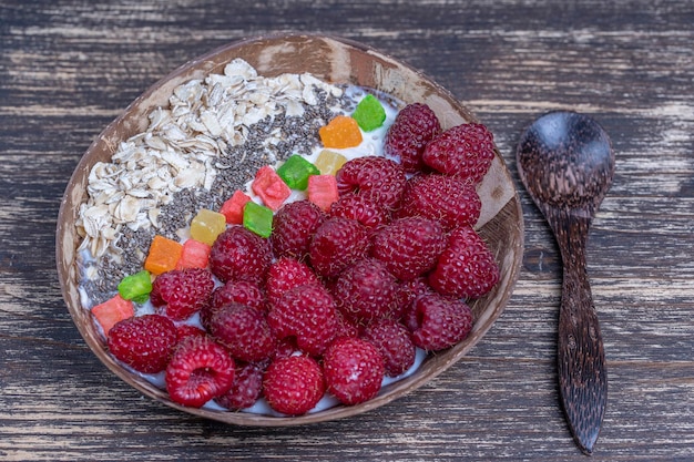 Smoothie in coconut bowl with raspberries oatmeal candied fruit and chia seeds for breakfast close up The concept of healthy eating superfood