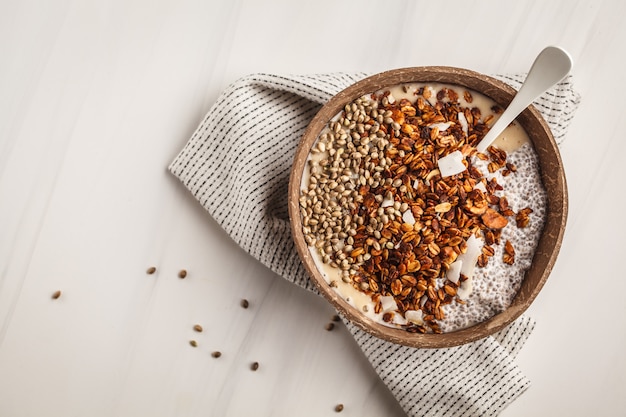 Smoothie kom met granola, chia pudding en hennepzaden in kom van kokosschaal.