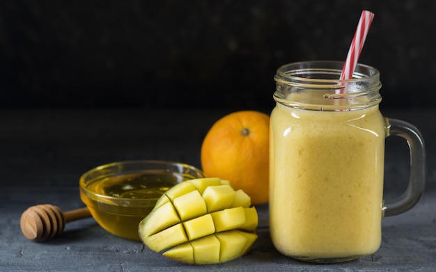 A smoothie of mango, banana, honey and cereal on a black surface