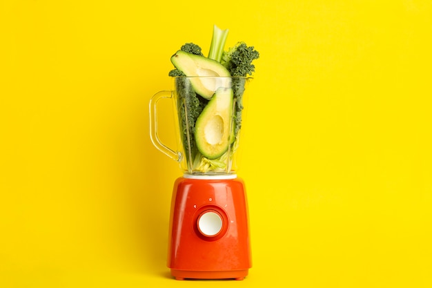 Ricetta smoothie. frullato verde di verdure (avocado, sedano, insalata di cale, spinaci) in un frullatore su uno sfondo giallo. concetto di disintossicazione di alimenti vegani e sani