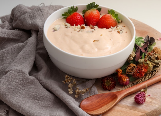 Smoothie van banaan, papaya en kokos vergezeld van Aardbeien en paranoten, in een witte kom en versierd met gedroogde bloemen.