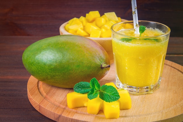 Smoothies mango with straw and mint in a glass beaker. Plate with sliced mango.