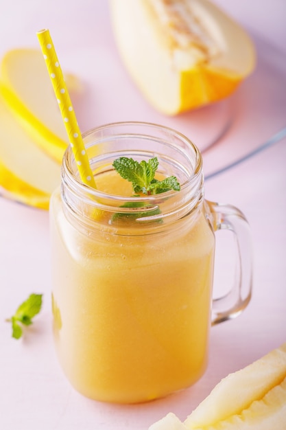 Smoothies prepared from ripe melon in a glass jar with mint and fruits on a wooden table