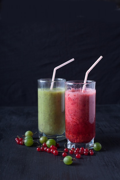 Smoothies of red currants and gooseberries stand on a on a black wooden table