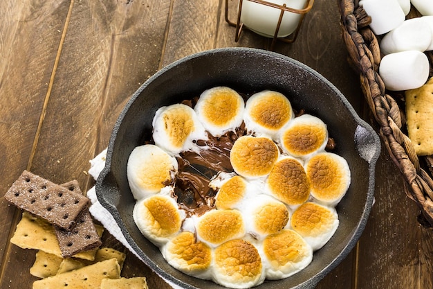 Smores dip prepared with large marshmallows in cast iron pan.