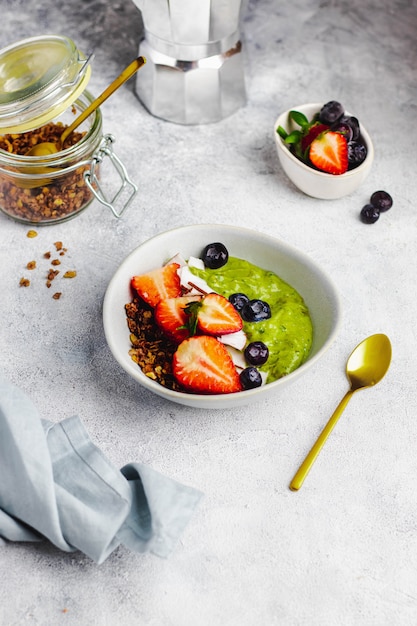 Smothie bowl with avocado, banana, spinach, coconut milk with granola, blueberry, strawberry and coconut chips. healthy breakfast concept. food for immunity boosting. top view with copyspace