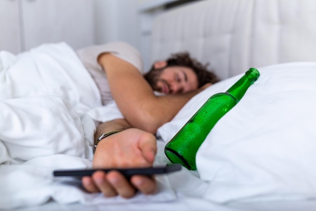 Sms'en terwijl dronken concept. Jonge man liggend in bed dodelijk dronken met lege fles drank. dronken met alcohol. Alcoholisme gewone dronkenschap verderfelijke gewoonte concept