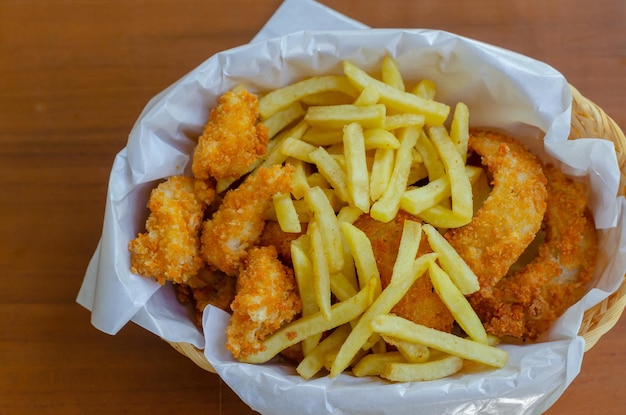 Snack Basket bevat friet, gebakken kipballetjes en uienringen geïsoleerd door houten achtergrond