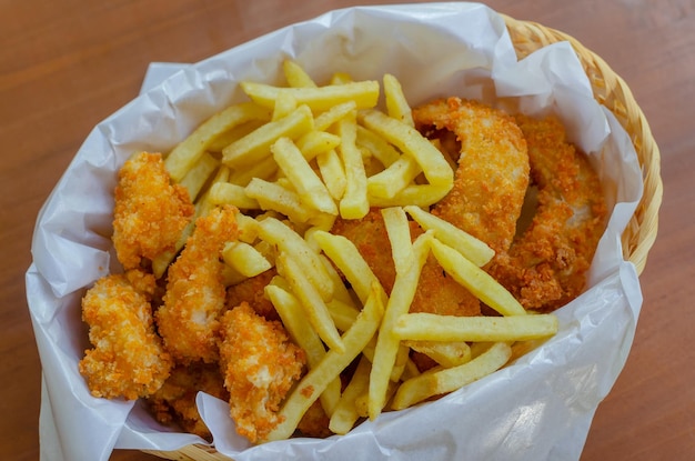 Snack Basket bevat friet, gebakken kipballetjes en uienringen geïsoleerd door houten achtergrond