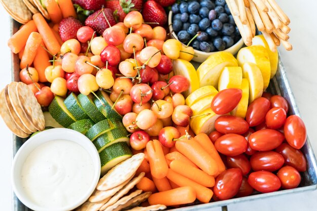 Snack board with fresh fruit, vegetables, crackers, and dips.