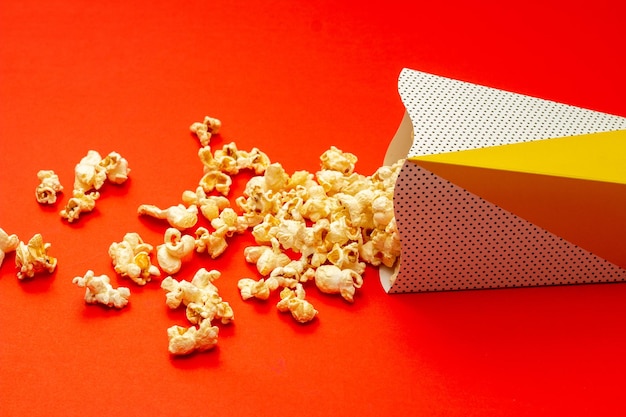 Snack concept Sweet popcorn spilled out from paper cup on red background